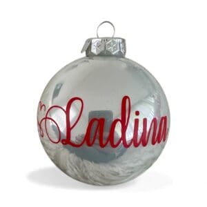 Glänzende silberweisse Weihnachtskugel 8 cm mit rotem personalisiertem Namensschriftzug „Ladina“ vor hellem Hintergrund.