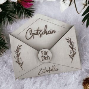 personalisierter Holz-Gutschein Umschlag mit Gravur „Gutschein“, „Für Dich“ und „Zeiterfüller“, umgeben von winterlich-weihnachtlicher Dekoration und Blumen auf flauschigem Untergrund.
