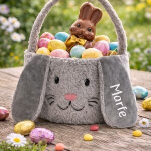 Personalisierter Osternest Kinder aus grauem Plüsch, gefüllt mit Ostereiern und Schokohase, auf Holztisch im Garten